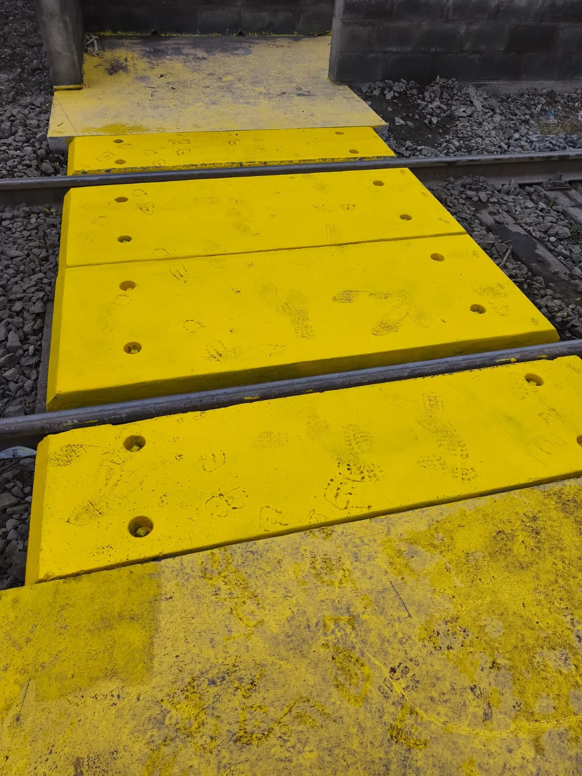 Losetas de hormigón amarillas instaladas entre los rieles de un cruce ferroviario real, con sus perforaciones de anclaje a la vista