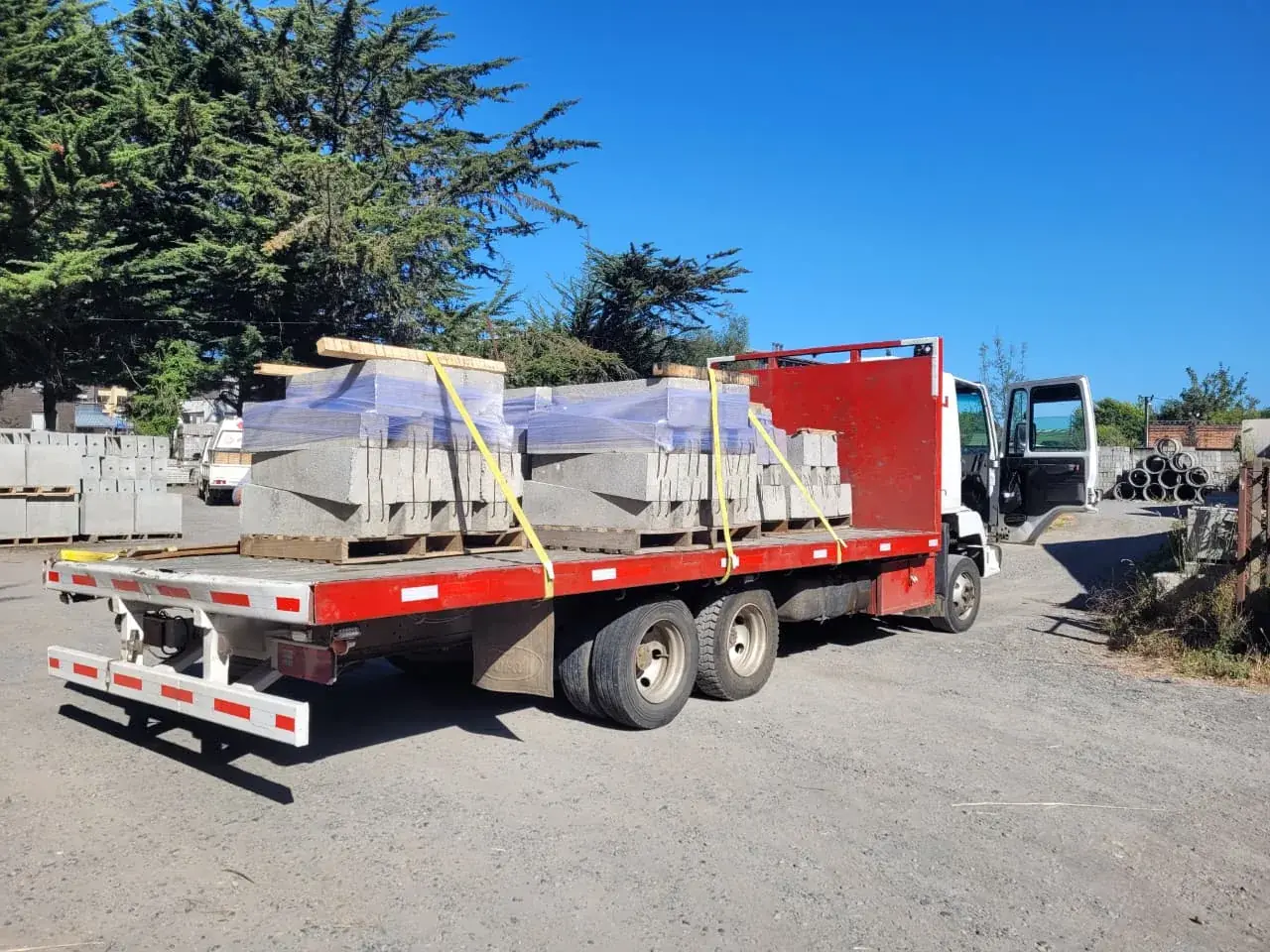 Camión de plataforma con piezas prefabricadas de hormigón sobre pallets, amarradas con eslingas y aseguradas para su traslado